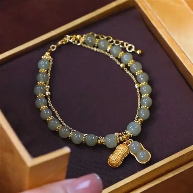 Goldenes Armband mit grünen Perlen und Erdnussanhänger in Schmuckschatulle.
