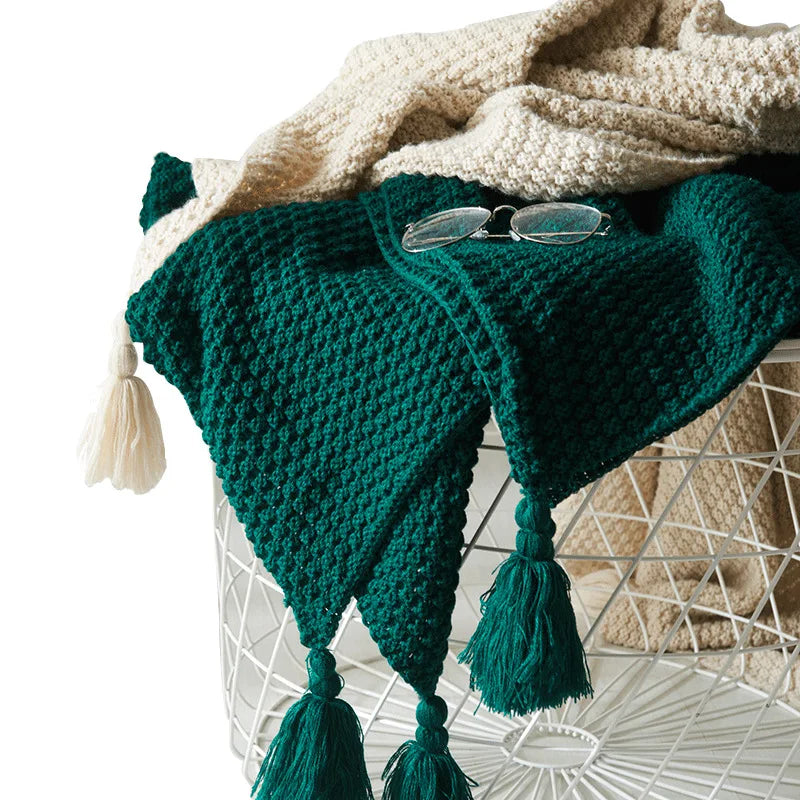 Grüne Strickdecke mit Quasten auf weißem Korb, gemütliche Wohnaccessoires, handgefertigt.