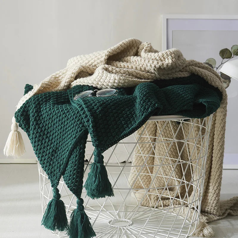 Grüner Strickplaid mit Quasten auf weißem Drahtkorb, dekorative Decke, Wohnzimmer Accessoire.