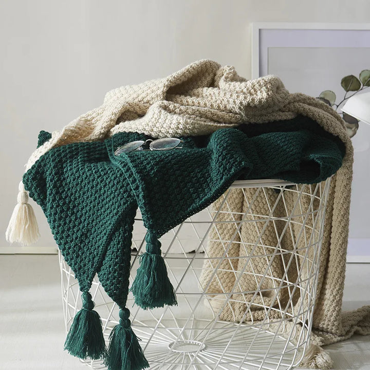 Grüner Strickplaid mit Quasten auf weißem Drahtkorb, dekorativer Wohnaccessoire.