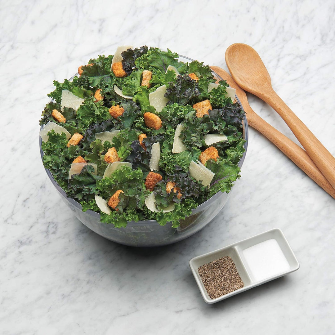 Grüner Salat mit Croutons und Parmesan in Glasschüssel auf Marmortisch, Holzlöffel daneben.