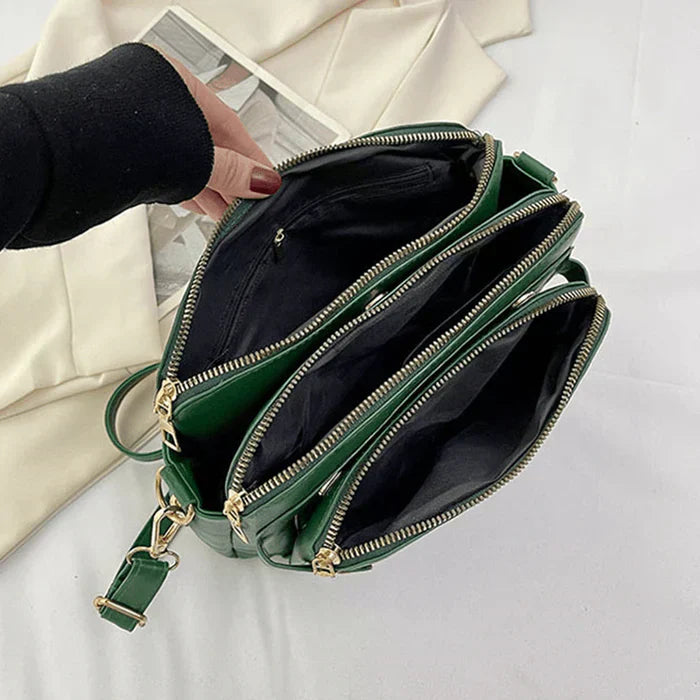 Grüne Leder-Crossbody-Tasche mit mehreren Fächern und goldenen Reißverschlüssen.