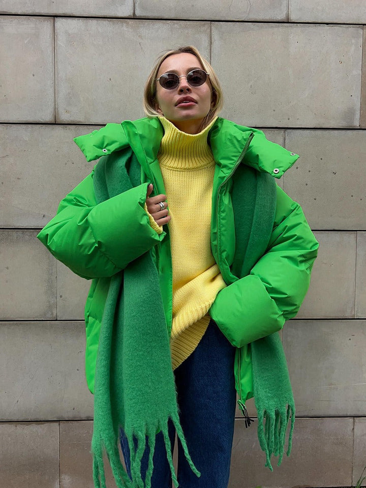 Frau in grüner Daunenjacke, gelbem Rollkragenpullover, grüner Schal, Sonnenbrille, Jeans.