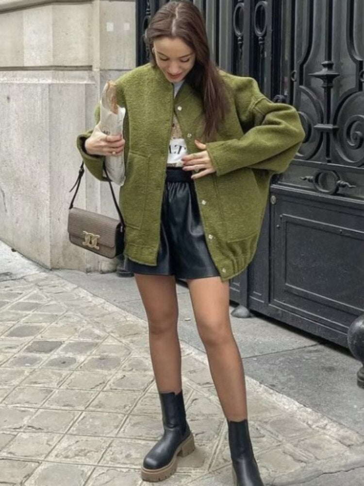 Frau in grüner Jacke, schwarzem Lederrock und Stiefeln, hält Baguette, modischer Streetstyle.