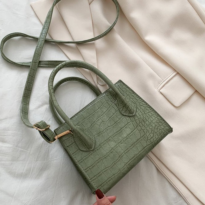 Grüne Krokodilleder-Handtasche mit Schulterriemen auf beigem Blazer, modisch, elegant.
