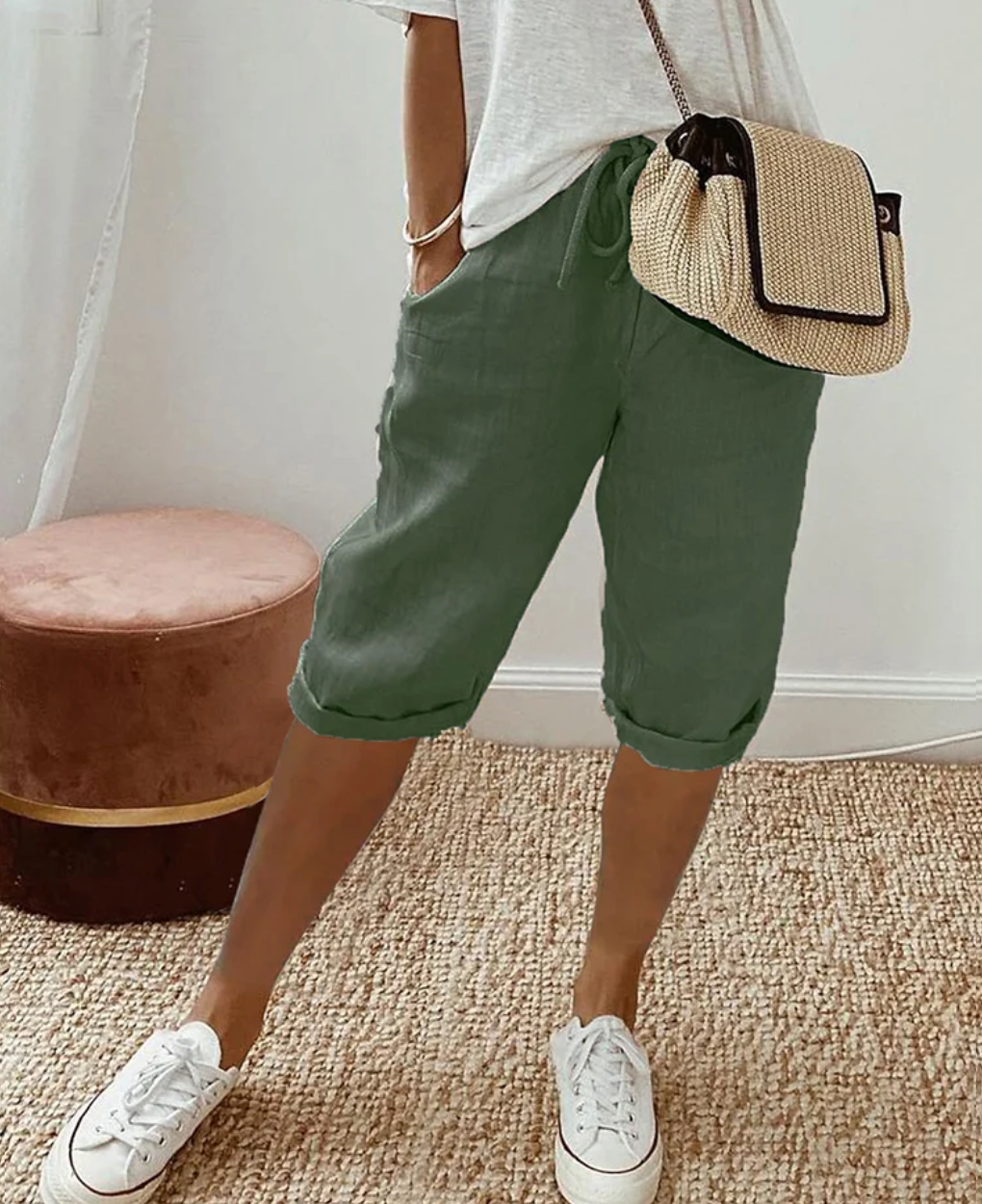 Frau in grüner Leinenhose, weißem T-Shirt, Strohtasche, weiße Sneaker, modisch, lässig.
