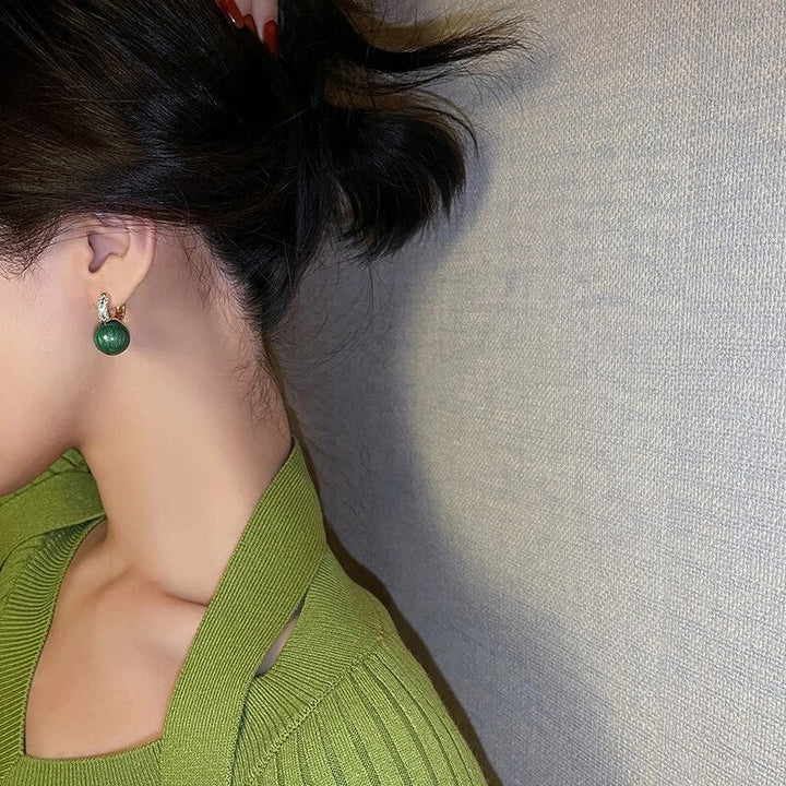 Frau mit grünen Ohrringen und grünem Pullover, eleganter Schmuck, Modeaccessoire.
