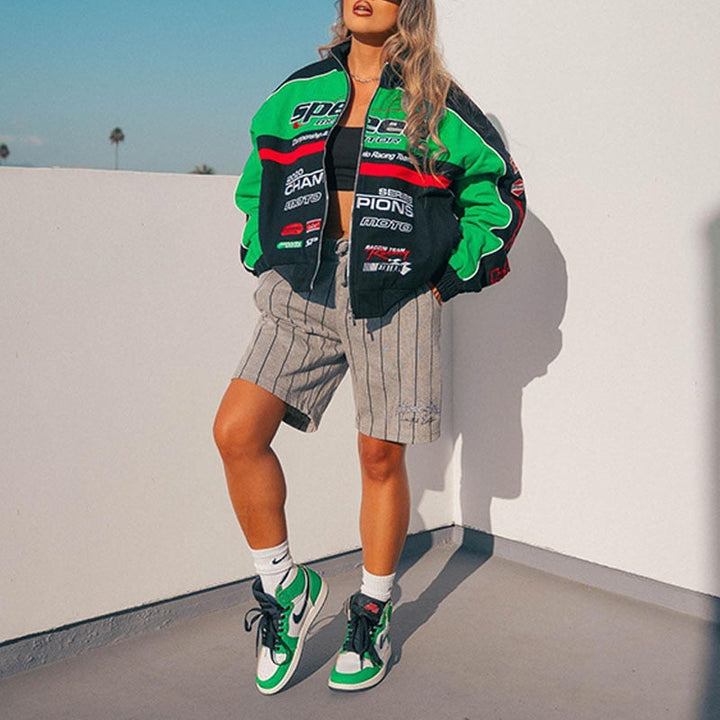 Frau in grüner Rennjacke und gestreiften Shorts, trägt grün-weiße Sneakers, urbaner Stil.