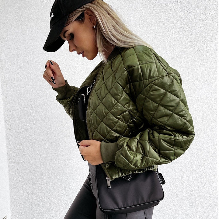 Frau in grüner Steppjacke, schwarzer Kappe und Tasche, modischer Streetwear-Look.