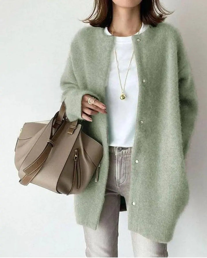 Frau in grüner Strickjacke, weißem T-Shirt, grauer Jeans, beige Handtasche, modisch, elegant.