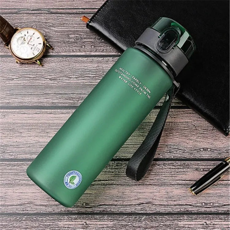 Grüne Edelstahl-Wasserflasche mit Trageschlaufe auf Holztisch, ideal für Outdoor-Aktivitäten.