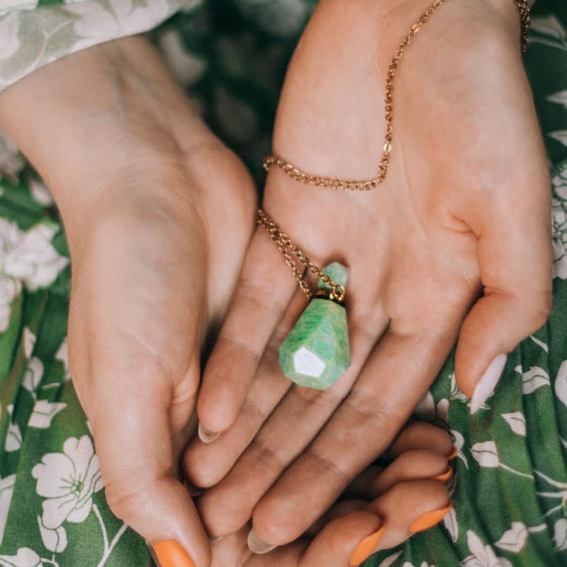 Frau hält grünen Edelstein-Anhänger an goldener Kette, Nahaufnahme, Schmuck, Modeaccessoire.