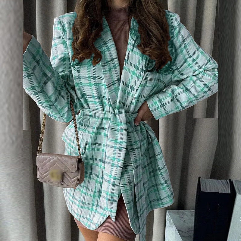 Frau in grün-kariertem Blazer mit Gürtel, braunes Kleid, kleine beige Umhängetasche.