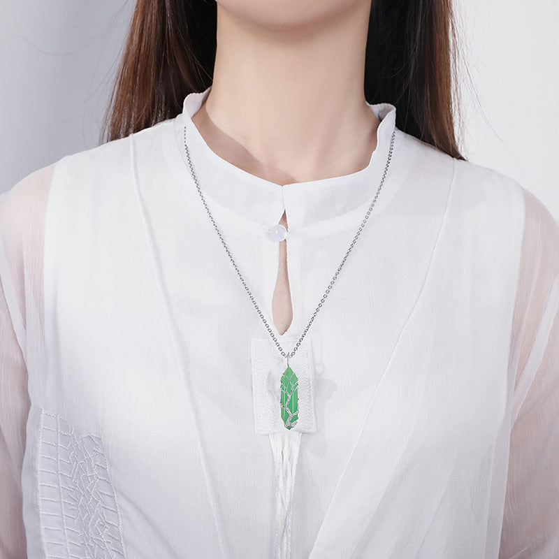 Frau mit weißer Bluse trägt silberne Halskette mit grünem Anhänger, eleganter Schmuck.