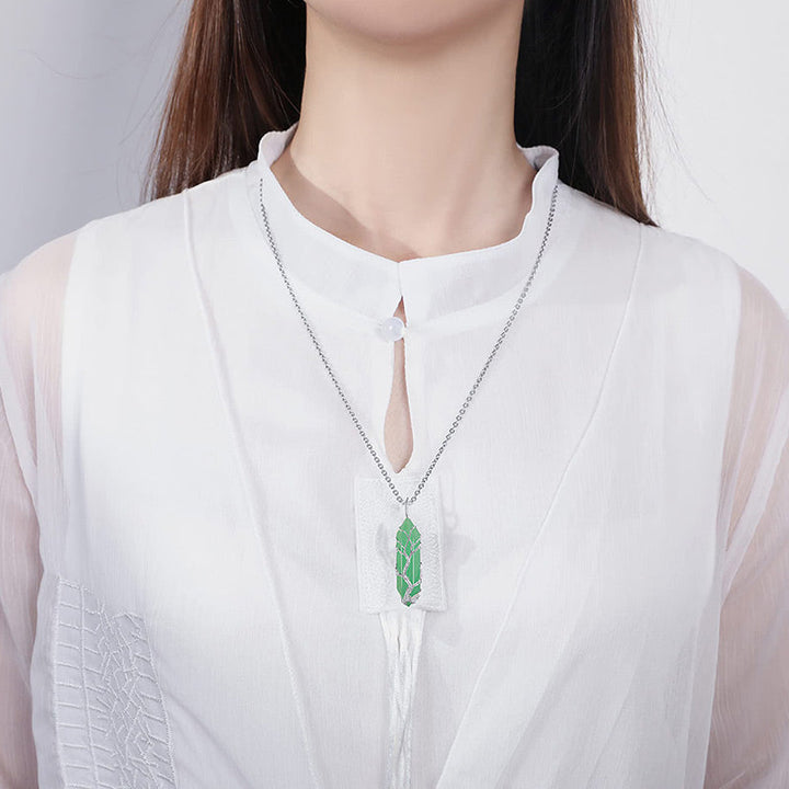 Frau mit weißer Bluse trägt silberne Halskette mit grünem Anhänger, eleganter Schmuck.