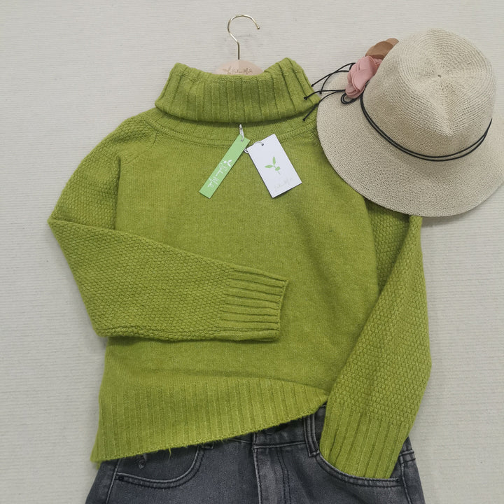 Grüner Rollkragenpullover aus Wolle mit Etikett, beige Hut, graue Jeans, flach gelegt.
