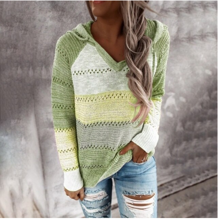 Frau in grünem Strickpullover mit Kapuze und zerrissenen Jeans vor grauem Hintergrund.