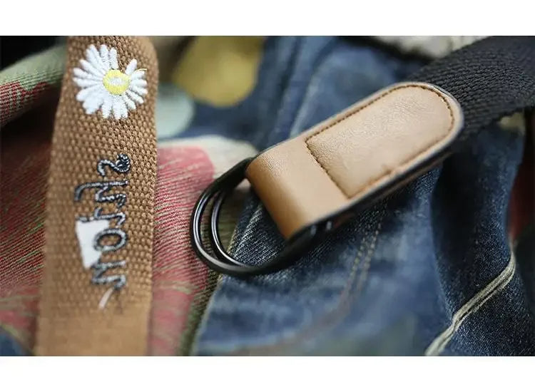 Brauner Stoffgürtel mit Gänseblümchen-Stickerei und Metallschnalle auf Jeanshintergrund.