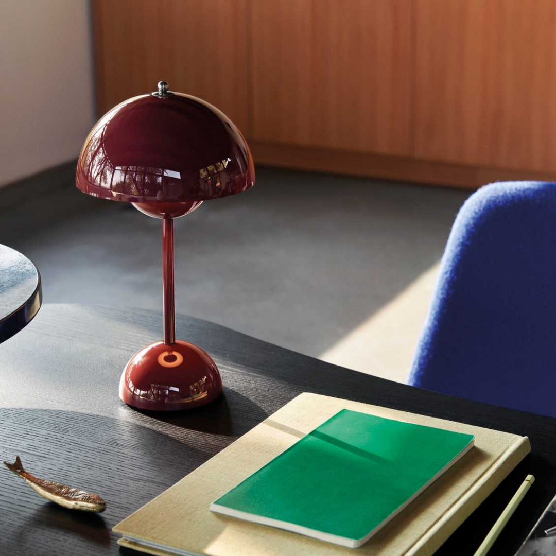 Rote Tischlampe auf Schreibtisch, modernes Design, neben Notizbuch und Stift, Innenraum.