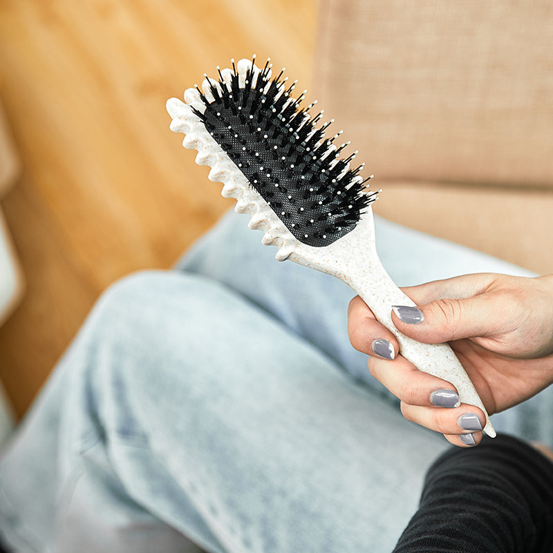 Person hält weiße Haarbürste mit schwarzen Borsten, ergonomisch, auf Jeanshintergrund.