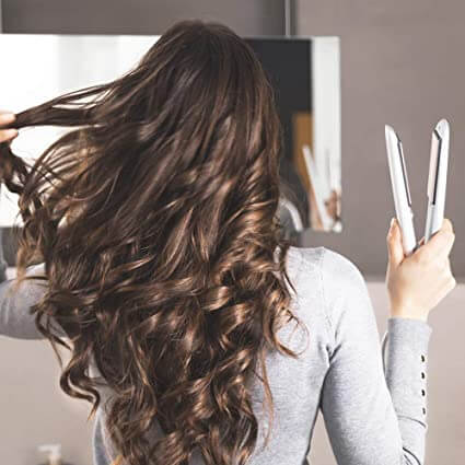 Frau mit Locken, hält weißen Haarglätter, Haarstyling, glattes Haar, Friseurwerkzeug.