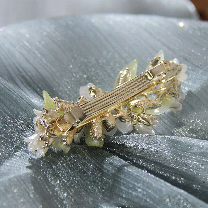 Goldene Haarspange mit Blumenmuster, Perlen und Strasssteinen auf grünem Stoff.