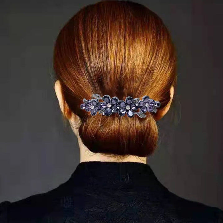 Frau mit braunem Haar, eleganter Haarklammer mit lila Blumen, Hochsteckfrisur, Rückansicht.