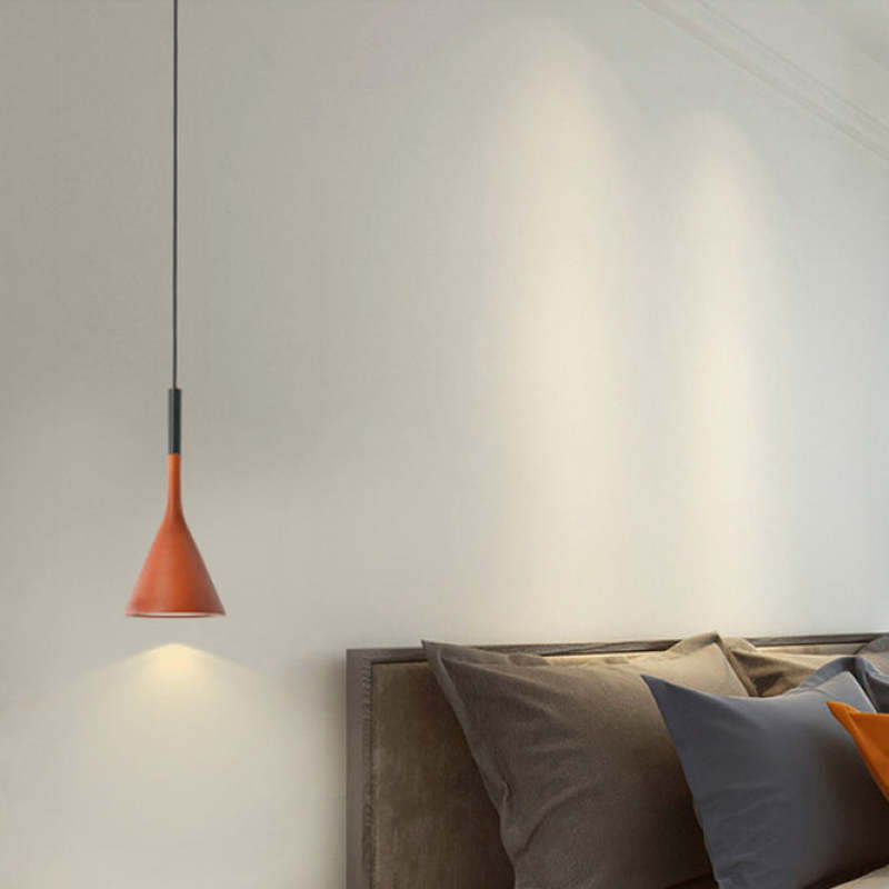 Moderne rote Pendelleuchte über einem Bett mit grauen Kissen, minimalistische Schlafzimmerbeleuchtung.