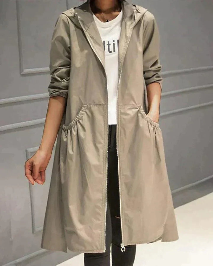 Béžový plášť s kapucí a zipem na modelce, ruka v kapse, bílé tričko a černé džíny 1