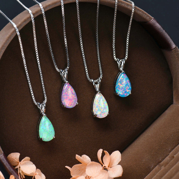 Vier Opal-Anhänger an Silberketten in Schmuckschatulle, bunte Edelsteine, elegantes Design.