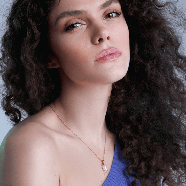 Frau mit lockigem Haar trägt blaues Oberteil und Perlenkette, Nahaufnahme, Modefotografie.