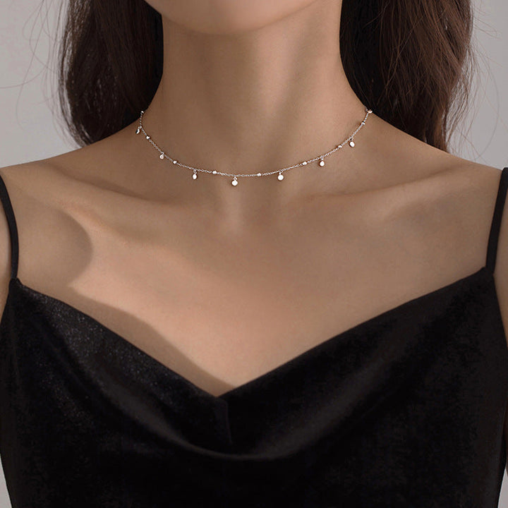 Frau mit schwarzem Kleid trägt elegantes, silbernes Perlenhalsband, minimalistisch, modisch.