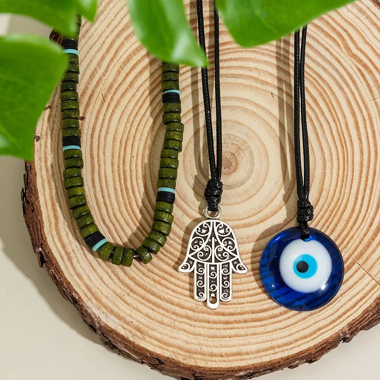 Grünes Perlenarmband, silberner Hamsa-Anhänger, blaues Nazar-Amulett auf Holzplatte.