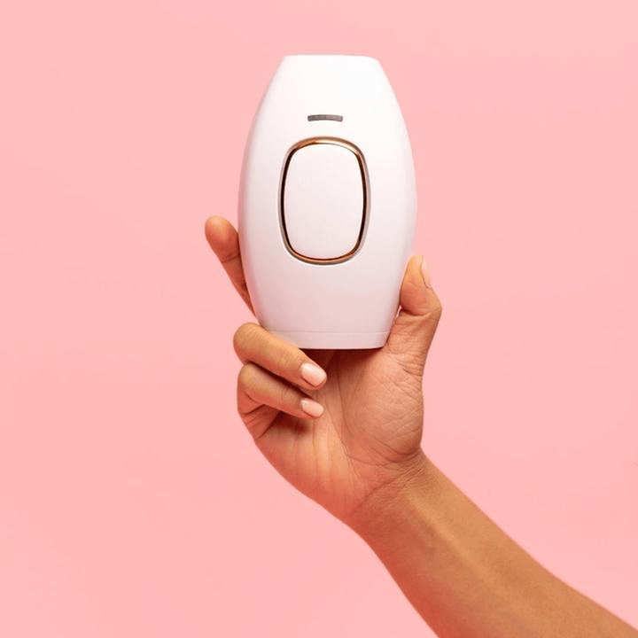 Hand hält weißes IPL-Haarentfernungsgerät vor rosa Hintergrund.