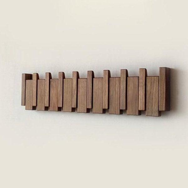 Pohled zepředu na tmavý dřevěný věšák se složenými háčky, upevněný na světlé zdi 4