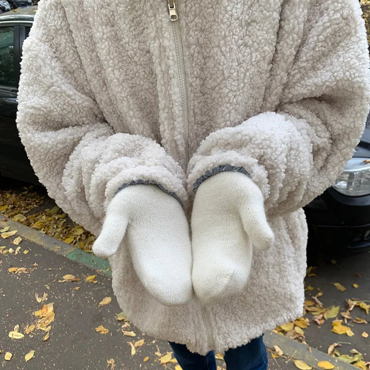 Person in weißem Teddyfellmantel und weißen Handschuhen im Herbst auf Straße.