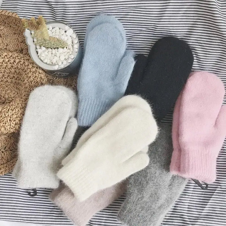 Verschiedene gestrickte Fäustlinge in Pastellfarben auf gestreiftem Hintergrund.