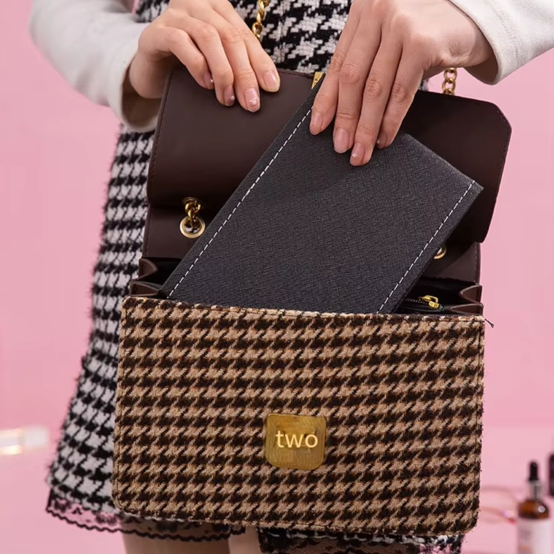 Frau mit Hahnentritt-Handtasche, braun, goldene Details, elegantes Design, rosa Hintergrund.