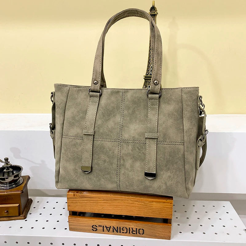 Graue Damenhandtasche aus Leder mit Trageriemen auf Holzkiste im modernen Design.