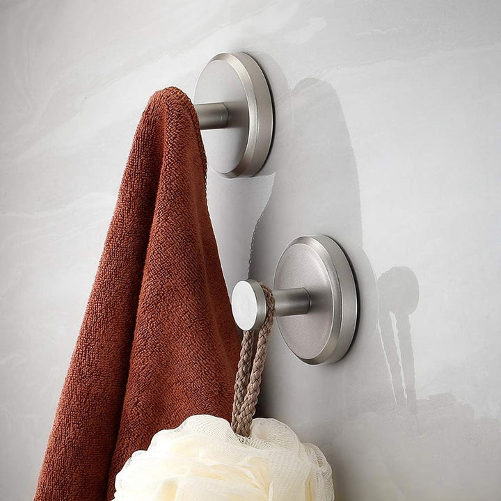 Zwei Edelstahl-Handtuchhaken an Wand mit braunem Handtuch und Duschschwamm.