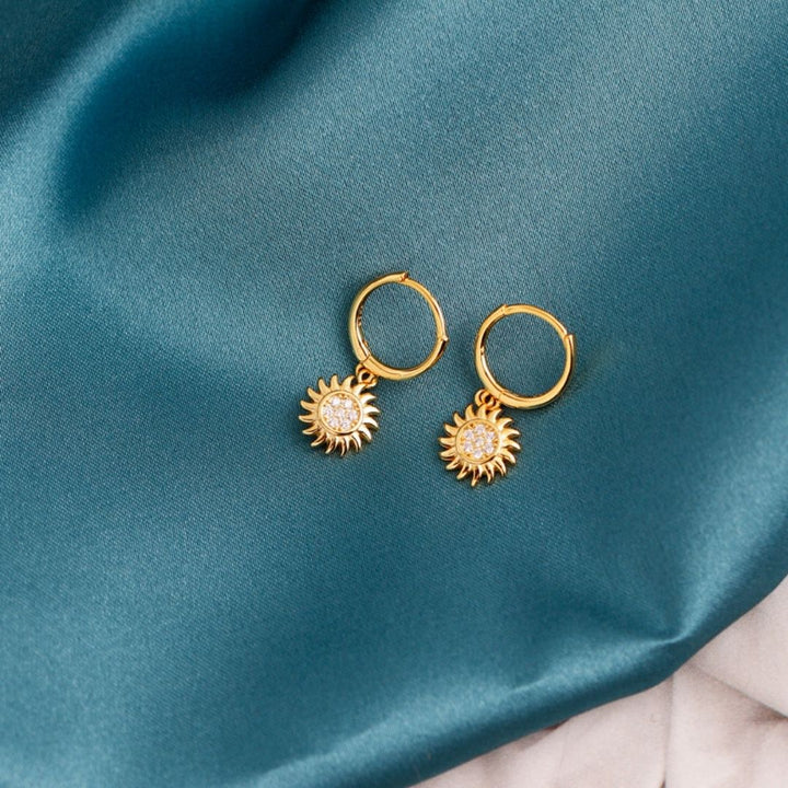 Goldene Sonnen-Creolen-Ohrringe auf blauem Stoff, Schmuck, modisch, elegant.