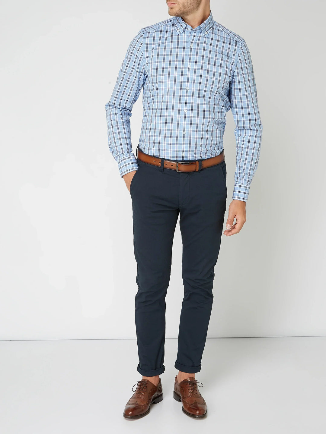 Mann in kariertem Hemd und blauer Hose, brauner Ledergürtel, elegante braune Lederschuhe.