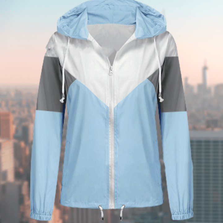 Hellblaue Windjacke mit Kapuze, Reißverschluss und grauen Akzenten vor Stadtlandschaft.