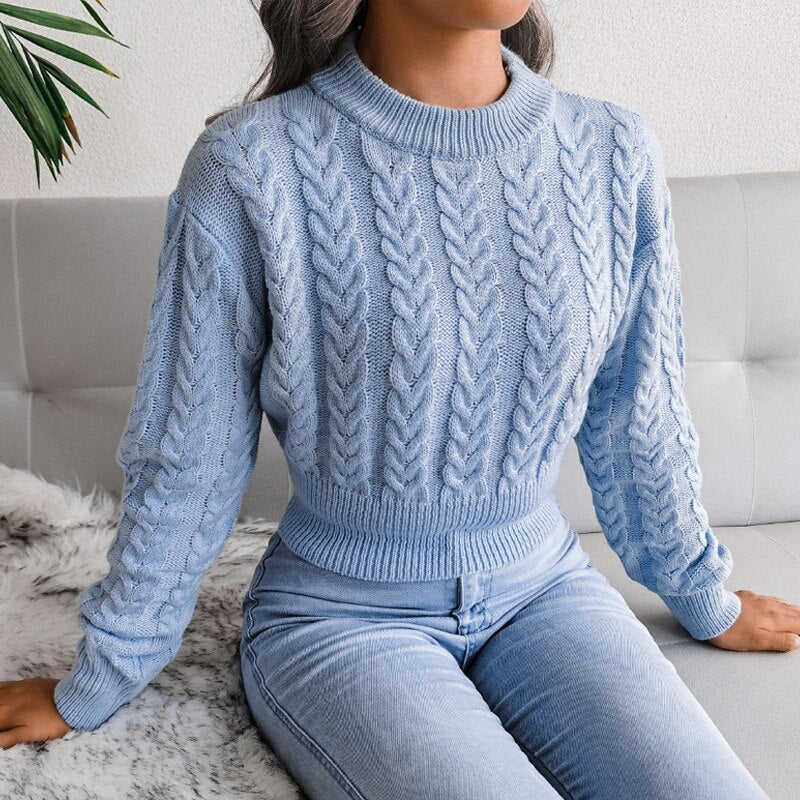 Frau in hellblauem Zopfmuster-Pullover und Jeans auf Sofa sitzend.