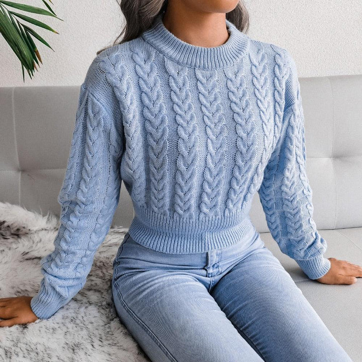 Frau in hellblauem Zopfmuster-Pullover und Jeans auf grauem Sofa, modisch, gemütlich.