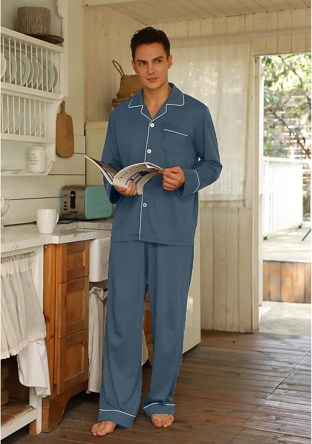 Mann in blauen Baumwoll-Pyjamas liest Zeitschrift in gemütlicher Küche.