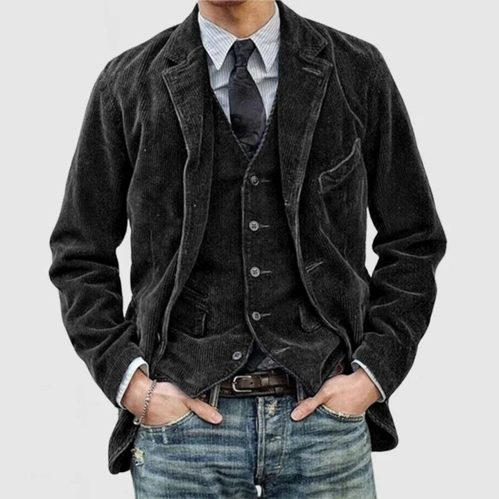 Mann in schwarzem Cord-Sakko mit Weste, gestreiftem Hemd und Jeans, modischer Herrenstil.