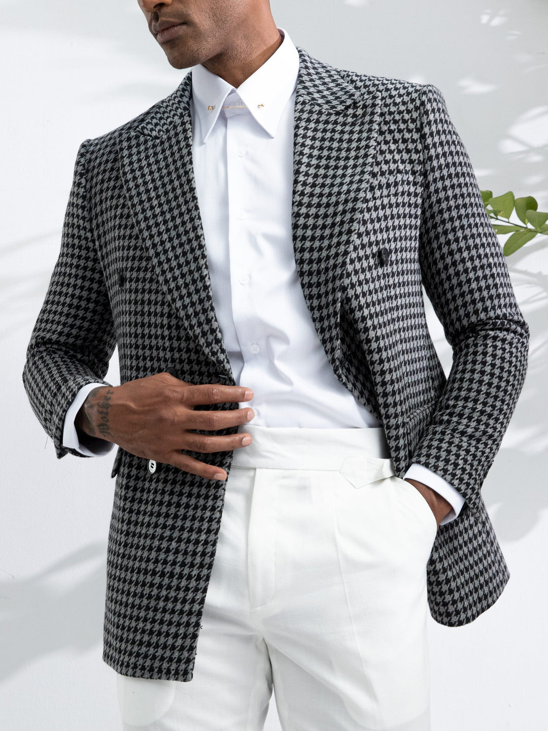 Mann im eleganten Hahnentritt-Blazer, weißes Hemd, weiße Hose, stilvolle Herrenmode.