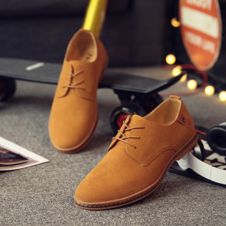 Braune Herren-Lederschnürschuhe auf grauem Teppich neben Skateboard und Lichtern.