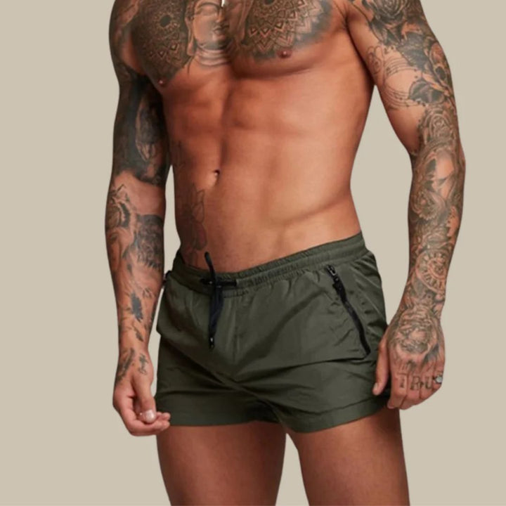 Mann in olivgrüner Sportshorts, tätowiert, Fitnessmode, Herrenbekleidung, athletischer Körper.